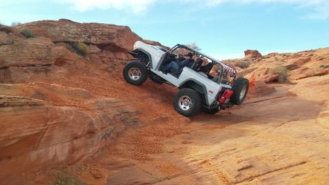1979 Ford Bronco - A modified white Ford Bronco navigates a challenging off-road course on a sunny day.