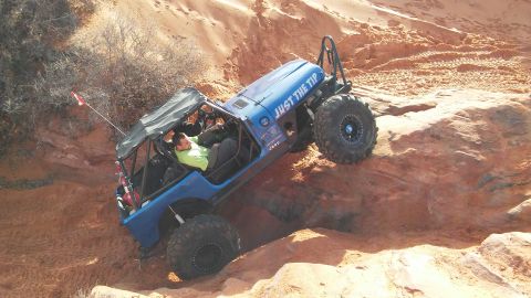1979 Ford Bronco - A blue Jeep navigates a challenging off-road trail with steep sandy and rocky terrain.