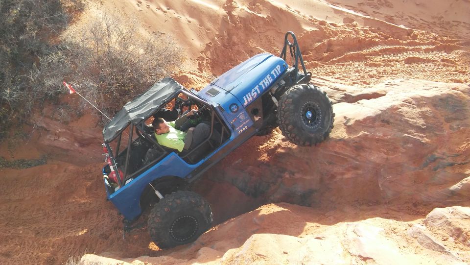 Blue Jeep with large tires climbing a rocky, sandy incline. Text on the hood says 'JUST THE TIP'