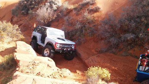 1979 Ford Bronco - A white Ford Bronco navigates a sandy trail with rocky outcrops and sparse vegetation.