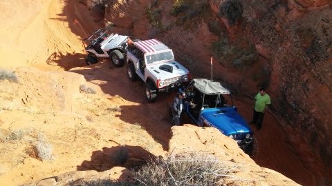 1979 Ford Bronco - Multiple off-road vehicles, including a Ford Bronco, traverse a challenging sandy trail in a canyon.
