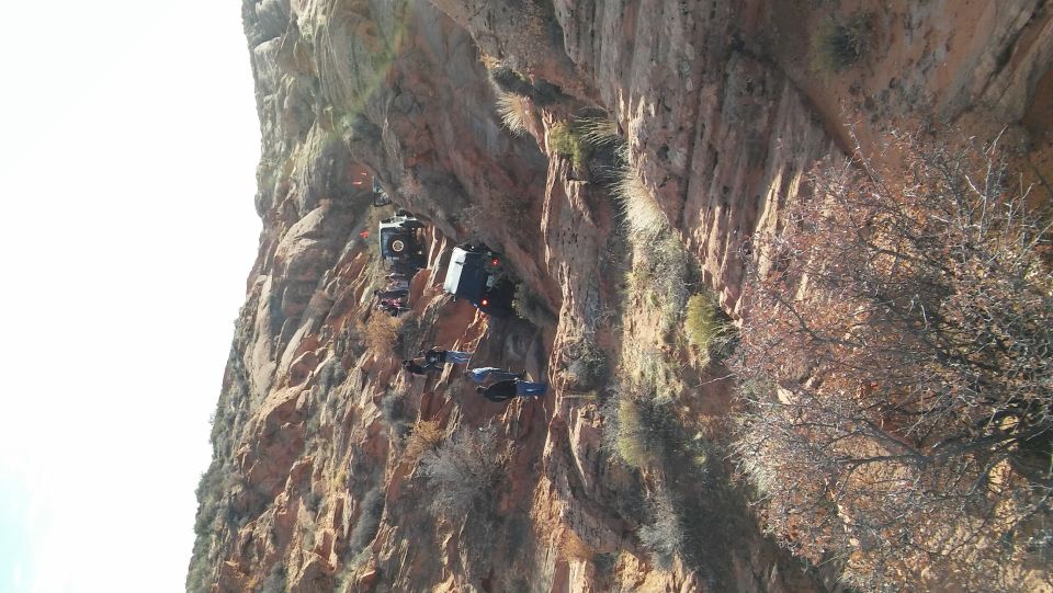 Multiple off-road vehicles precariously positioned on a steep, rocky cliff face under a bright sky