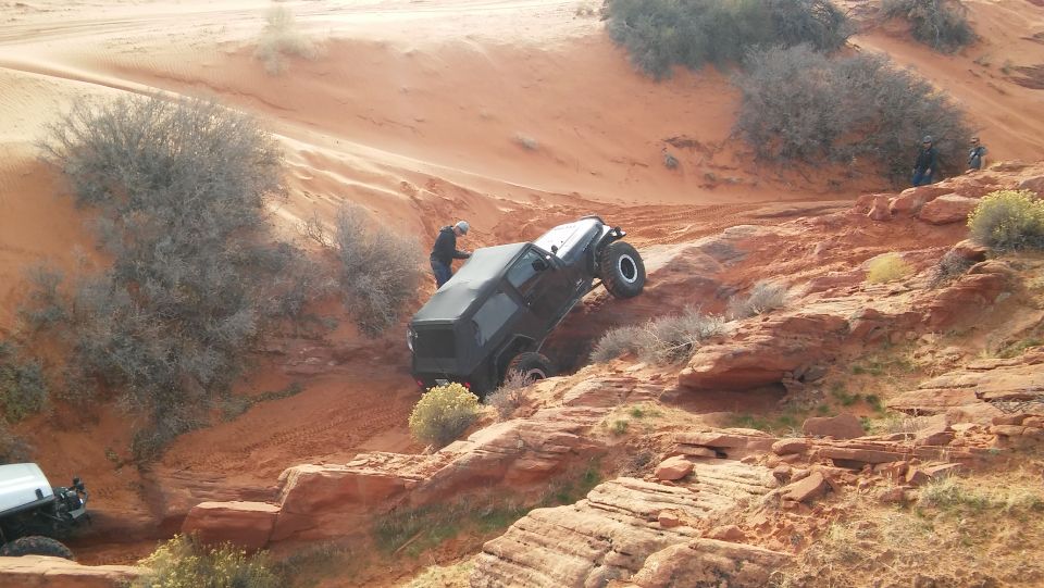 Black Jeep Wrangler climbing a rocky, sandy hill with a white Jeep visible below