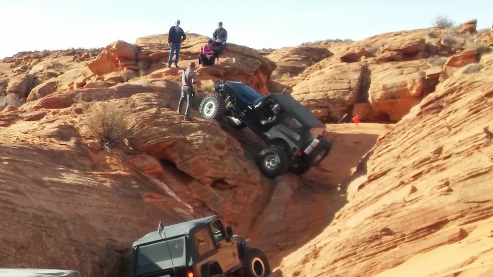 Two dark-colored Jeeps navigate a steep, rocky incline under a clear sky
