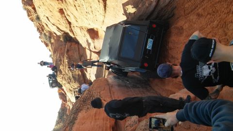1979 Ford Bronco - A group of people watch as a black SUV navigates a challenging off-road trail on a sandstone cliff.
