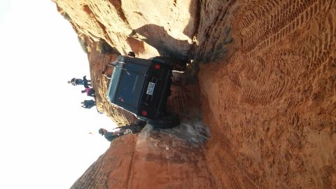 1979 Ford Bronco - Jeep Wrangler navigating a tight spot on a rocky trail, with onlookers observing the maneuver.