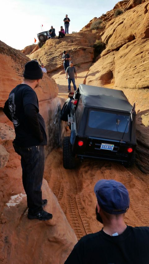 1979 Ford Bronco - Off-roaders navigate a steep, sandy canyon with multiple Jeeps and spectators.