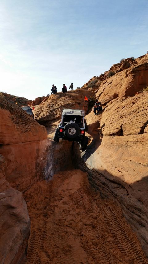 1979 Ford Bronco - Multiple off-road vehicles navigate a tight canyon trail with spectators on the surrounding rock formations.