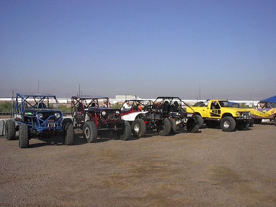 Row of five off-road rock crawler rigs with roll cages and big tires parked on gravel lot