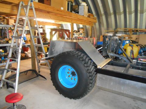 1992 Ford Bronco - A custom off-road vehicle chassis is shown with a large tire and bright blue wheel in a workshop setting.