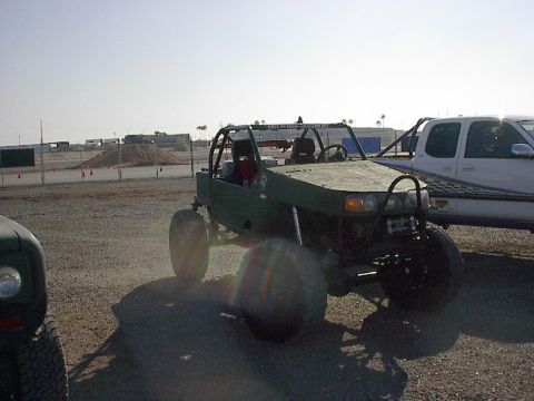 1984 Ford Bronco - A custom-built off-road buggy with a roll cage sits parked on a dirt lot next to a pickup truck.