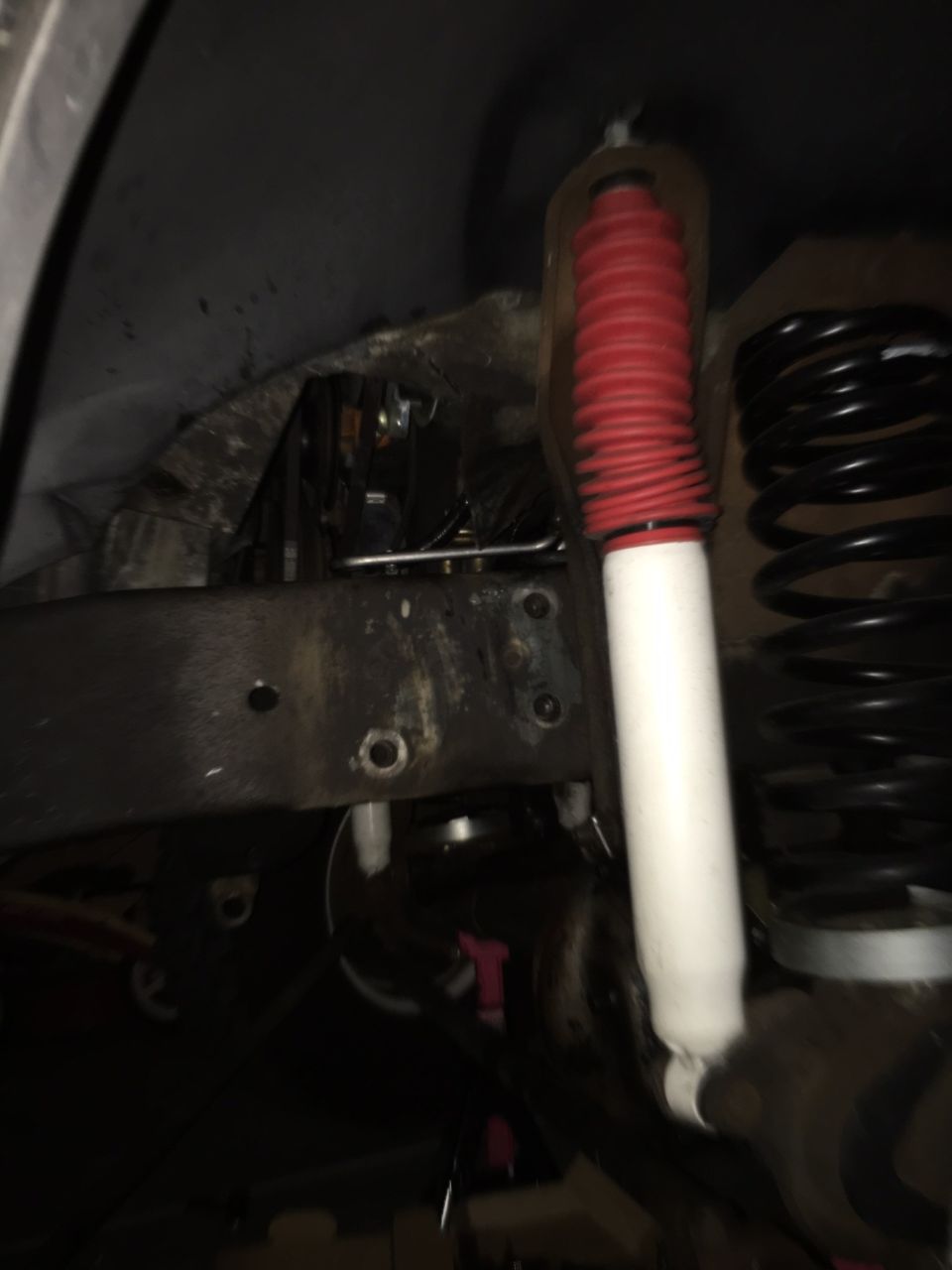 Close-up of a vehicle's front suspension with a red-booted shock absorber and black coil spring