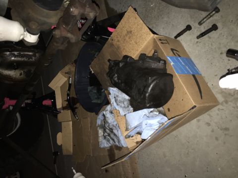 1978 Ford Bronco - A black steering gear box sits in a cardboard box, surrounded by oily rags and automotive parts.