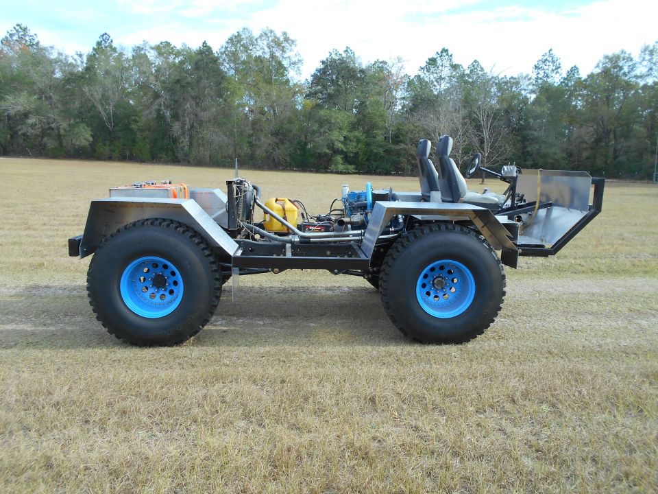 Custom off-road vehicle with exposed engine, blue wheels, and two seats, viewed from the side