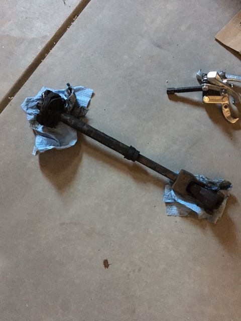 1978 Ford Bronco - A steering shaft with U-joints is shown resting on paper towels on a concrete floor, with a tool in the background.