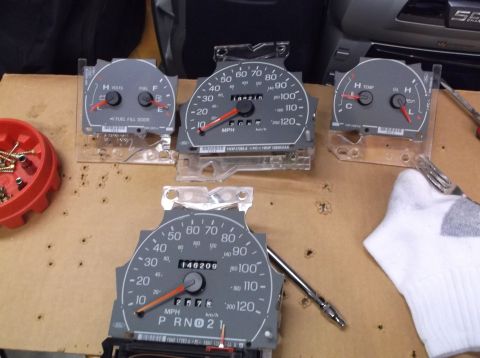 1999 Mercury Grand Marquis - Several vehicle instrument cluster gauges are laid out on a surface, along with screws and tools.
