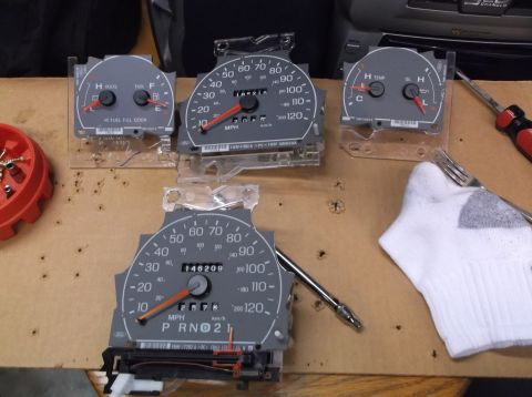 1999 Mercury Grand Marquis - Instrument cluster gauges from a 1999 Mercury Grand Marquis are laid out on a table, likely for installation or repair.