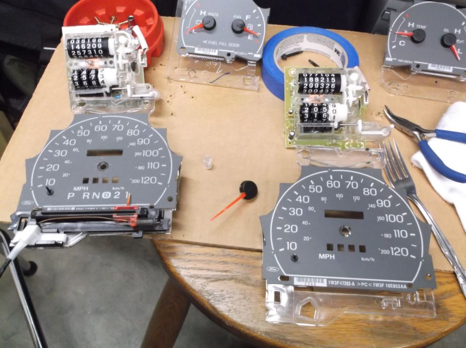 Disassembled car dashboard gauges and odometer components on a table, with tools nearby