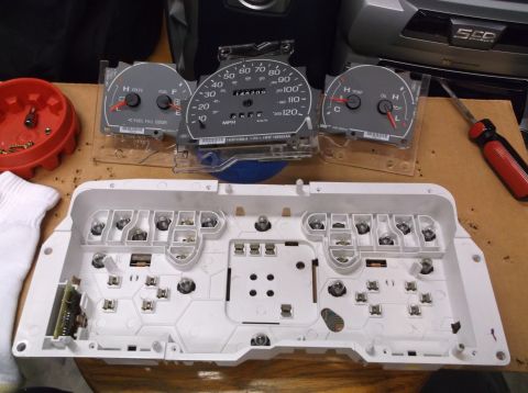 1999 Mercury Grand Marquis - The disassembled instrument cluster components are spread out on a workbench, ready for installation or repair.