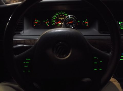 1999 Mercury Grand Marquis - The interior of a vehicle shows a dashboard with illuminated gauges and a steering wheel with integrated controls. A tachometer is mounted…