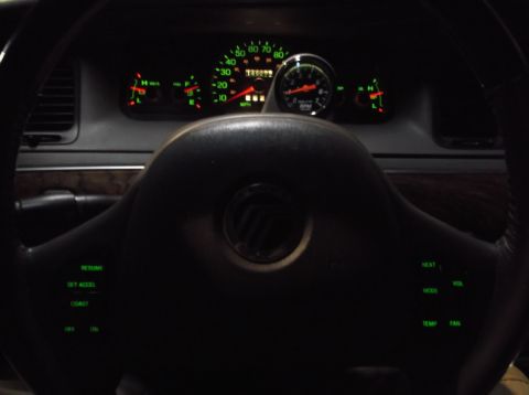 1999 Mercury Grand Marquis - The interior of a 1999 Mercury Grand Marquis shows the dashboard with illuminated gauges and a steering wheel with cruise control buttons.…