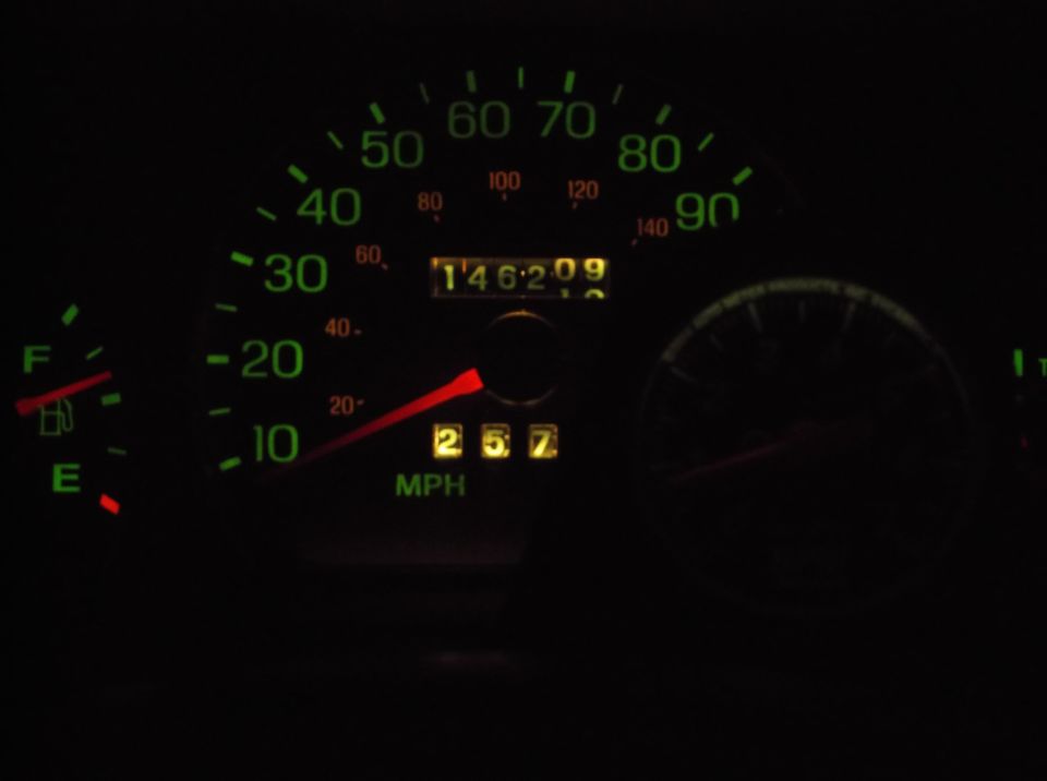Car dashboard at night showing speedometer, odometer, and fuel gauge.