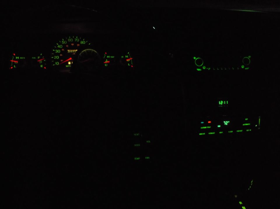 Car dashboard at night with illuminated gauges and climate controls. Speedometer reads 30 MPH, odometer reads 14557.