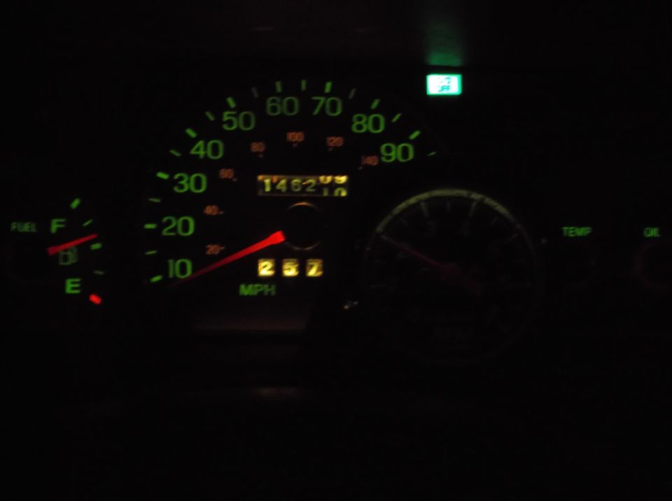 Car dashboard at night showing speedometer at 25 mph and odometer at 146210.