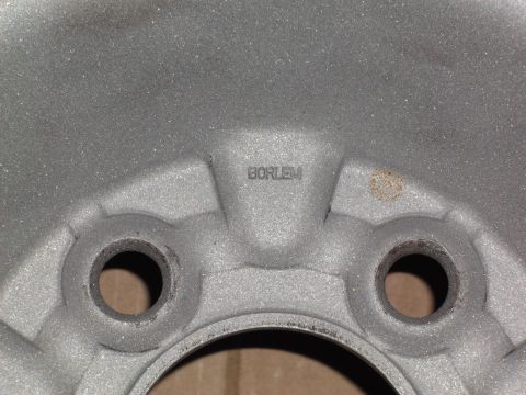 1999 Mercury Grand Marquis - A close-up view of a silver alloy wheel shows the embossed text "BORLEM" near the lug nut holes. There is a small rust spot visible on the…