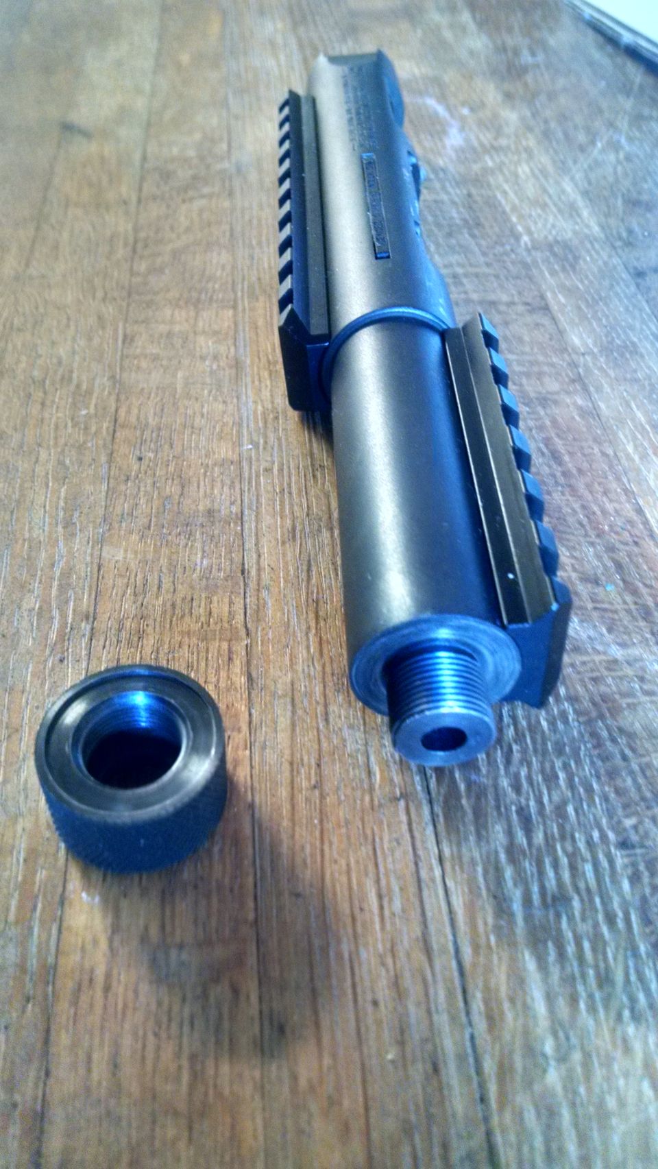 Threaded barrel with rails and a separate threaded cap on a wooden surface.