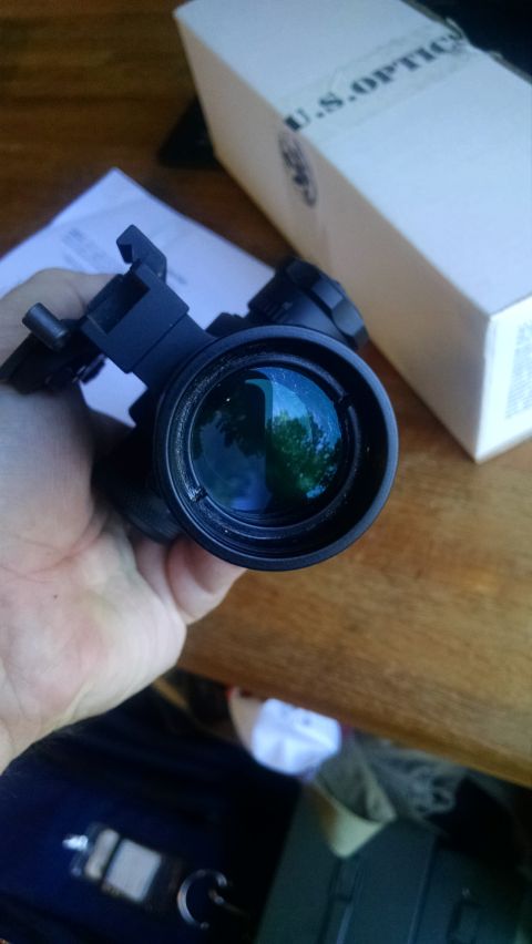 1996 Ford Bronco - A hand holds a black optical scope with a blue lens reflection. In the background is a white box with "U.S. OPTICS" printed on it.