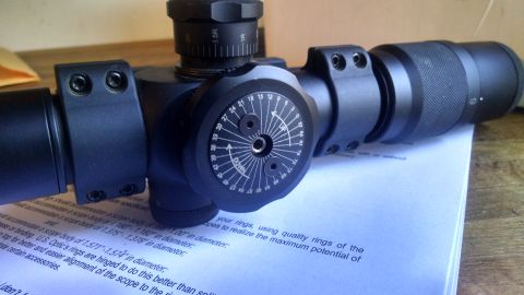 1996 Ford Bronco - A close-up view of a black rifle scope with adjustment turrets and markings. The scope is resting on a document with printed text.