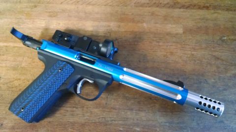 1996 Ford Bronco - A blue and silver custom pistol with a red dot sight is shown on a wooden surface. The pistol has a textured blue grip and a vented barrel…