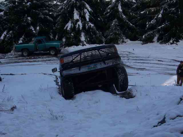 Dark Ford 4x4 with driving lights nosed into a snowbank on a snowy wooded trail