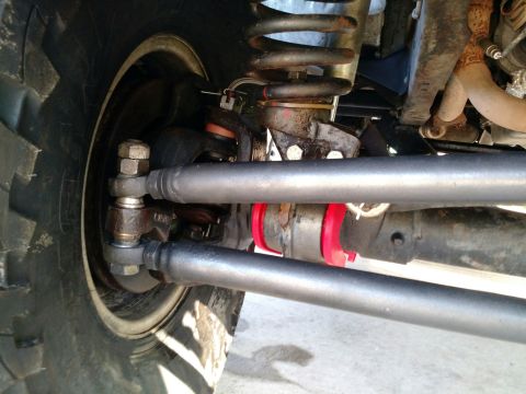 1992 Ford Bronco - Close-up view of a vehicle's steering linkage, prominent tie rods and red bushings, with a portion of a large tire visible.