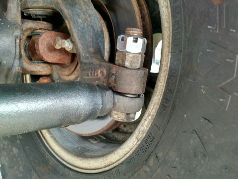 1992 Ford Bronco - Close-up view of corroded steering linkage components, including a tie rod end and nut, next to a tire.
