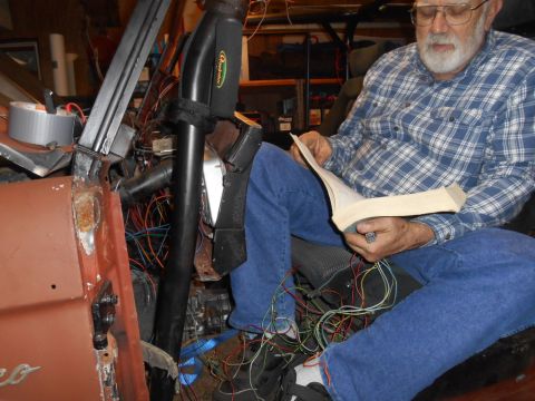 1972 Ford Bronco - A man consults a manual while surrounded by complex wiring within the interior of a vehicle undergoing restoration.