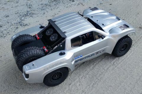 1986 Ford Bronco - A remote control rock racer sits on a sandy surface, its off-road tires and exposed rear suspension.