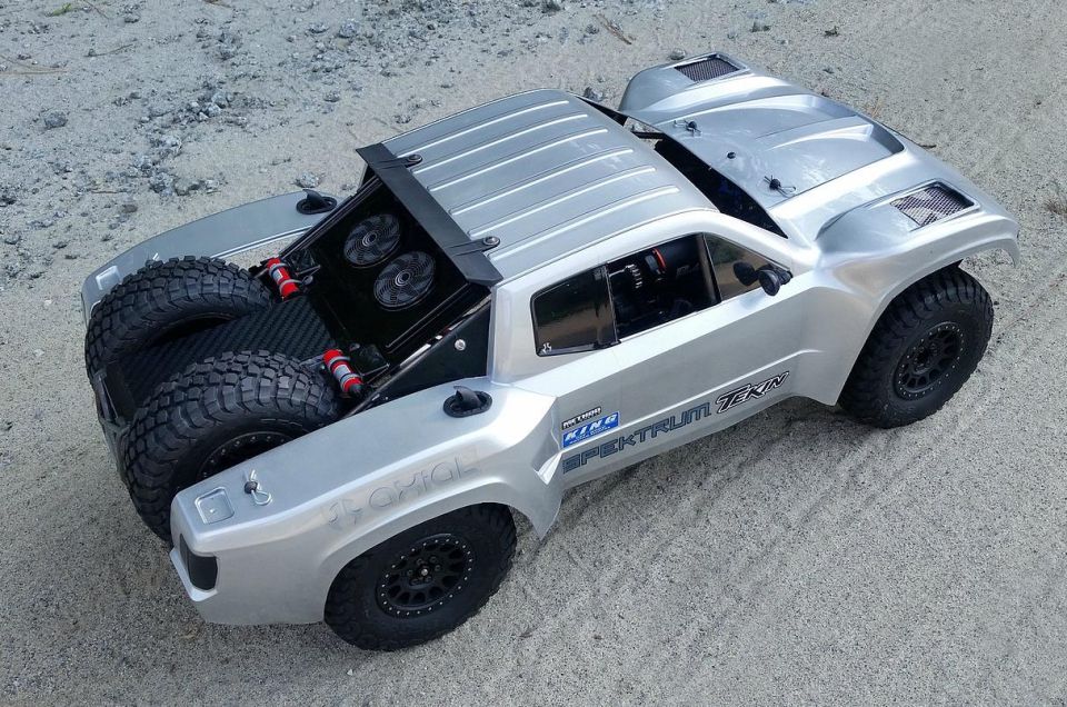 Silver remote control rock racer with two spare tires in the back. Has 'SPEKTRUM' and 'TEKIN' text on the side