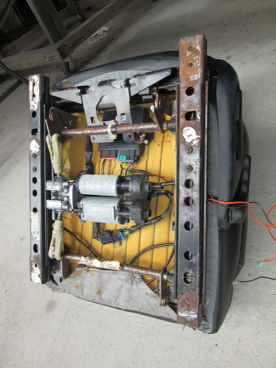 Car seat frame with exposed motors and wiring, yellow foam padding visible