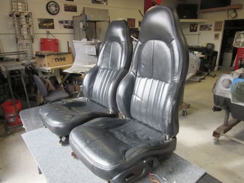Two black leather car seats with vertical stitching, viewed from the front in a garage