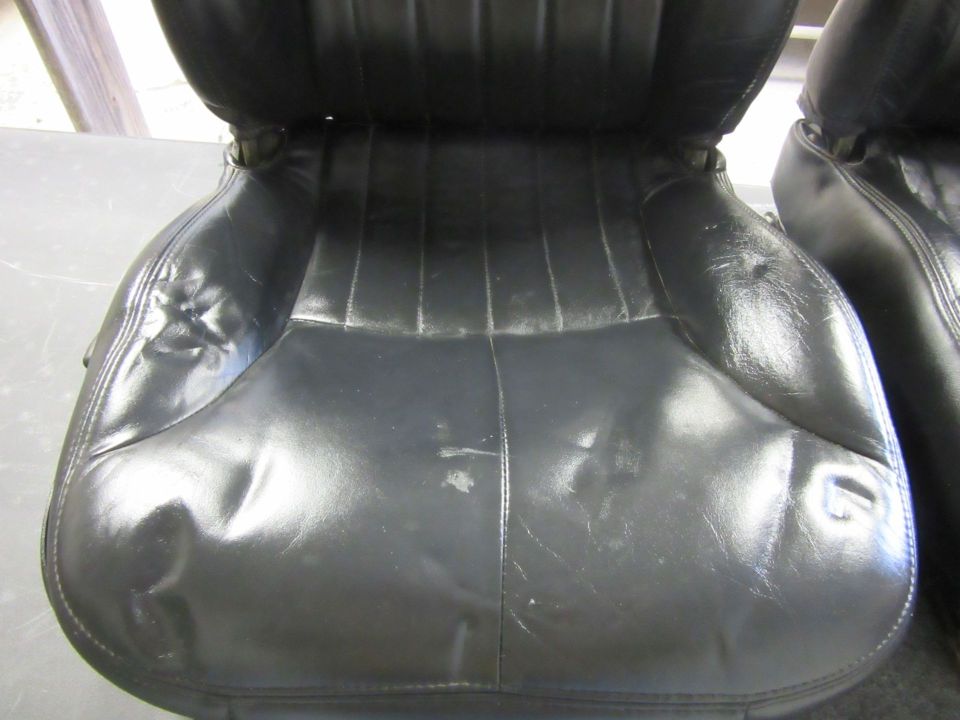 Black leather car seats with vertical stitching and visible wear
