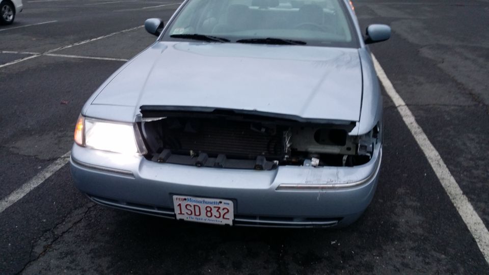 Front view of a light blue 2005 Mercury Grand Marquis with a damaged grille and missing headlights