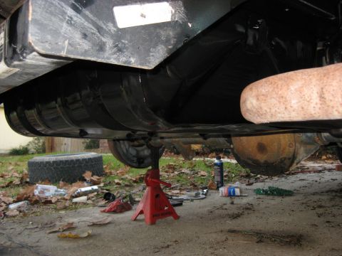 1994 Ford Bronco - The underside of a vehicle is shown, a fuel tank and exhaust system, with a red jack supporting the frame.
