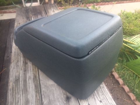 1986 Ford Bronco - A dark gray plastic center console with a hinged lid is shown resting on a wooden surface.