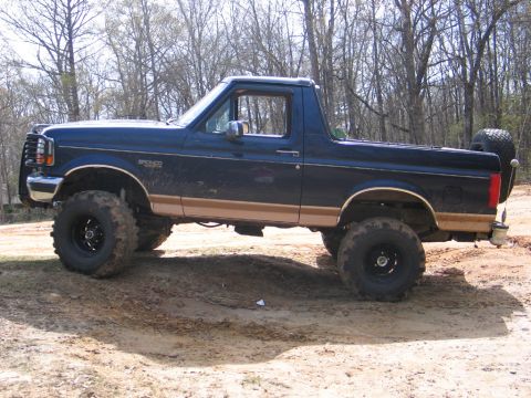 1995 Ford Bronco - This lifted 1995 Ford Bronco features a dark blue exterior with tan trim and a spare tire mounted on the rear.