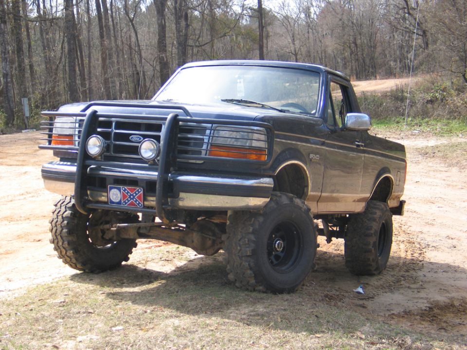 1995 Ford Bronco lifted with large tires and front bull bar, parked on dirt