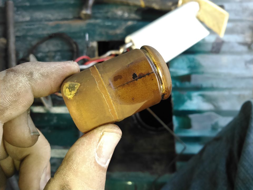 Dirty fuel pump strainer held by fingers, with a white filter element behind it