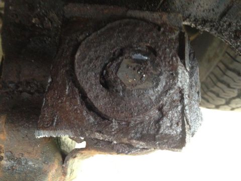 1995 Ford Bronco - Heavily corroded metal bracket with a visible bolt head, likely a vehicle undercarriage component.
