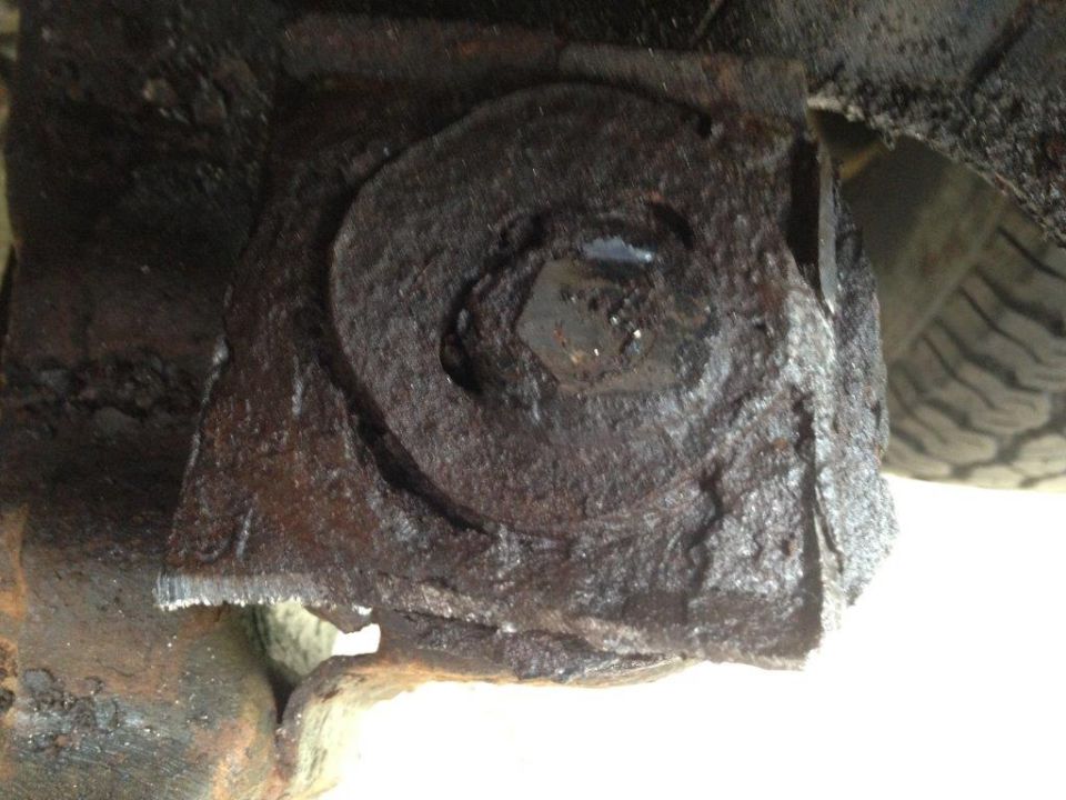 Close-up of a heavily rusted, bolted metal bracket, possibly part of a vehicle's suspension or frame